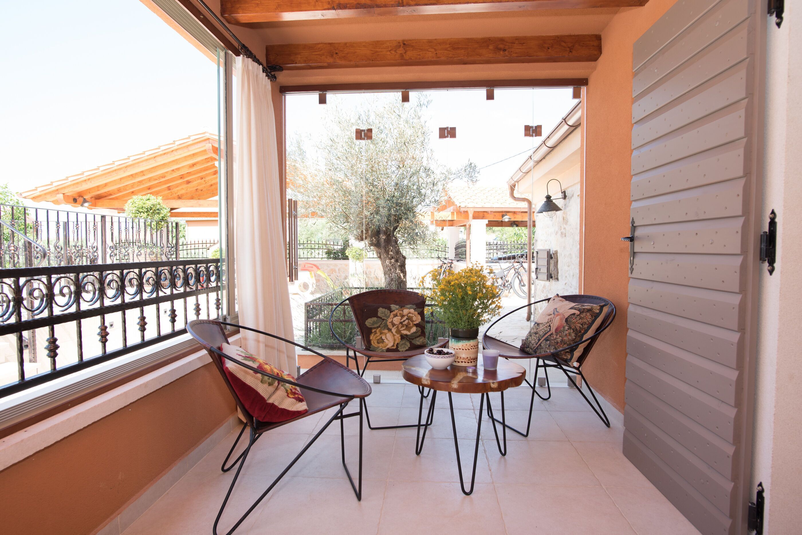An open balcony with a view of the street, two chairs, a small table, and a potted plant.