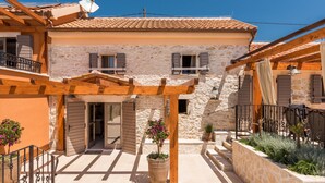 A traditional stone building with a tiled roof, wooden pergola, and a potted plant in the courtyard. - Villa Stone (Skradin)