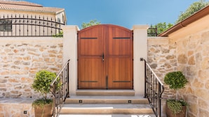 A wooden double door with a metal gate, flanked by stone walls and potted plants. - Villa Stone (Skradin)