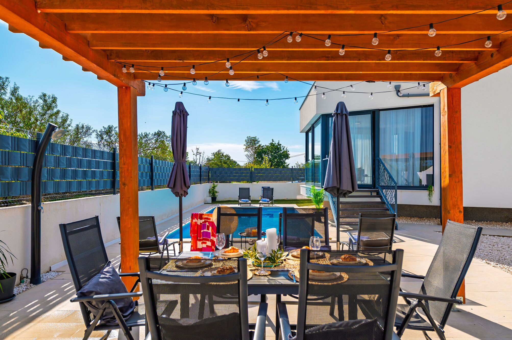 Un patio al aire libre con piscina, mesa de comedor, sillas y sombrillas.