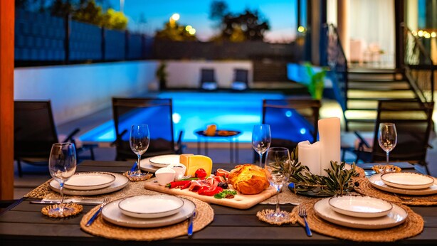 An outdoor dining area with a pool in the background, set tables with plates, glasses, and a variety of food items. - Villa Laurel (Rupe)