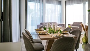 A dining area with a table set for four, large windows with curtains, and a modern chandelier. - Villa Laurel (Rupe)