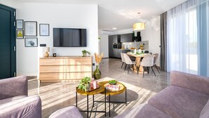 A modern living room with a flat-screen TV, wooden furniture, and a dining area with a chandelier. - Villa Laurel (Rupe)