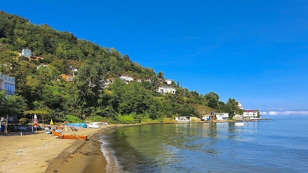 A beach with clear water, a sandy shore, and houses on a hillside. - Çeşmeönü Bungalov  (Persembe)