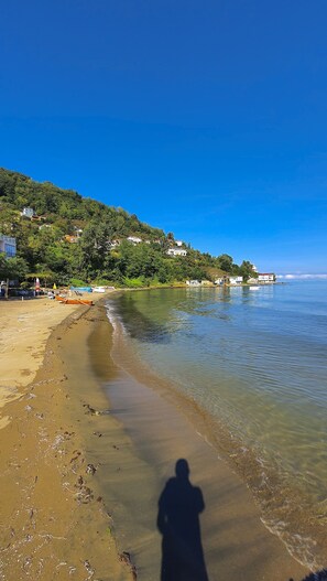 A beach with clear water, a sandy shore, and houses on a hillside. - Çeşmeönü Bungalov (Persembe)