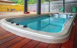 A hot tub with a wooden deck, stone walls, and green chairs.