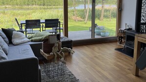 Una sala de estar moderna con un amplio ventanal corredizo que da a una terraza, un sofá gris, una mesita con una cesta y una chimenea.