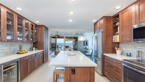 A modern kitchen with wooden cabinets, a central island, and stainless steel appliances. - Simply Stunning Condo, C202 is one of of the best! (Lahaina)
