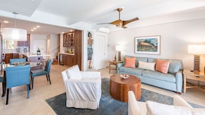A spacious living area with a sofa, coffee table, and chairs. There is a kitchen area with cabinets and a dining table. - Simply Stunning Condo, C202 is one of of the best! (Lahaina)