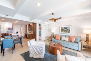 A spacious living area with a sofa, coffee table, and chairs. There is a kitchen area with cabinets and a dining table. - Simply Stunning Condo, C202 is one of of the best! (Lahaina)