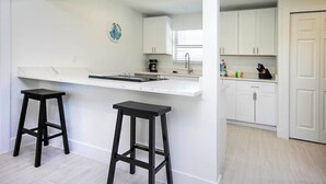 A modern kitchen with white cabinetry, a black countertop, and two black stools. - Blind Pass E103 - over 1500 sq ft ~ 8 person occupancy (Sanibel)