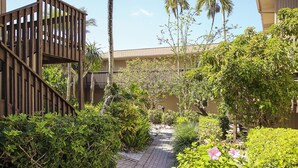 A pathway flanked by lush greenery and a wooden structure, leading to a building with a beige facade. - Blind Pass E103 - over 1500 sq ft ~ 8 person occupancy (Sanibel)