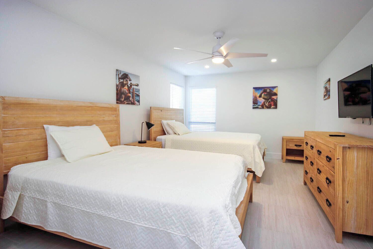 A bedroom with two beds, a ceiling fan, a TV, and wooden furniture.