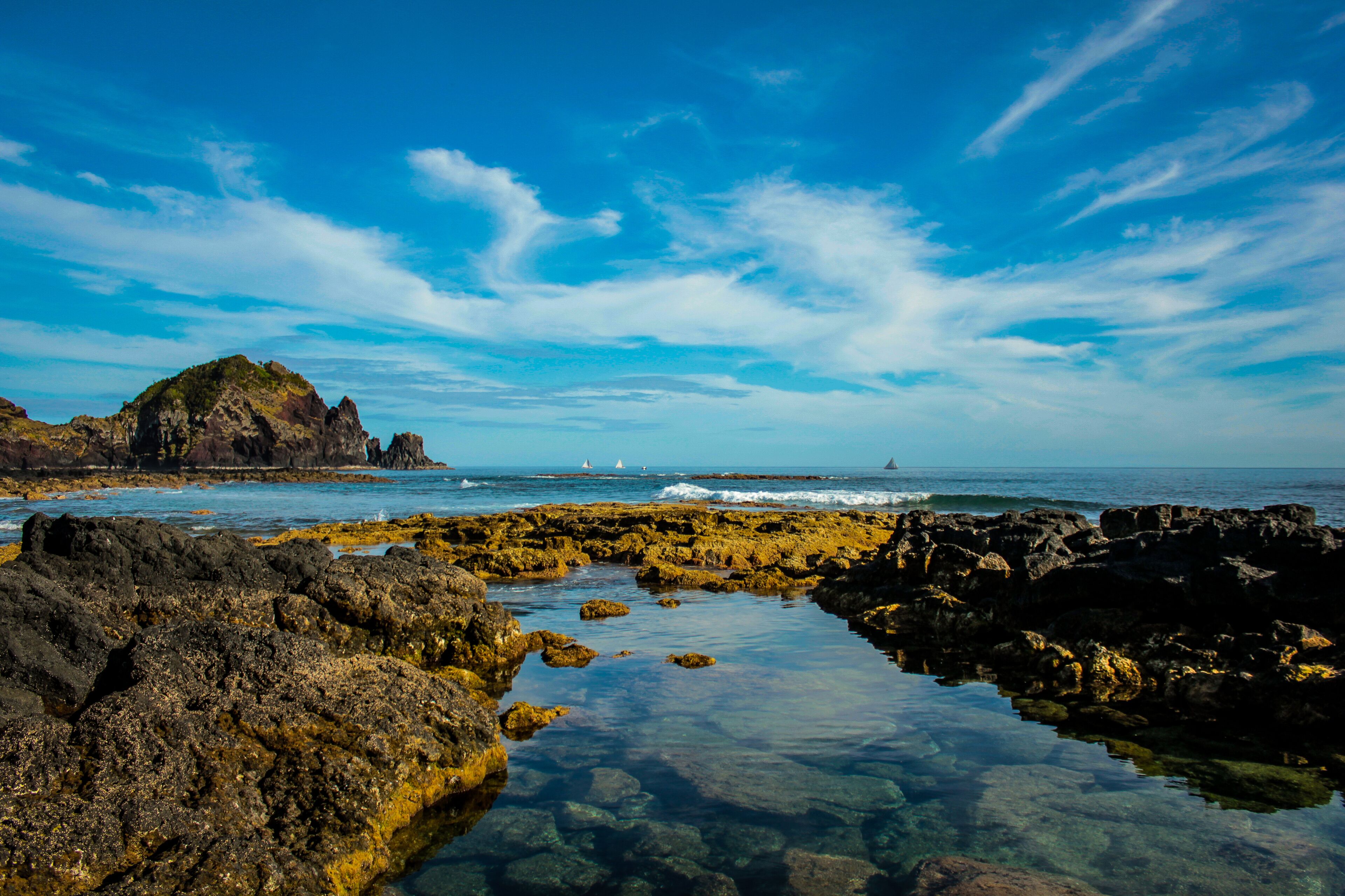 A rocky shoreline with clear water, a distant island, and a clear blue sky.