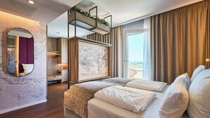 Habitación de hotel moderna con una cama grande, un mural con un mapa, una zona superior con una planta y un balcón con cortinas.