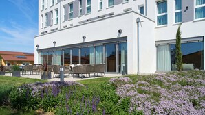 Un hotel moderno con fachada blanca, ventanas amplias y un jardín bien cuidado con flores moradas.