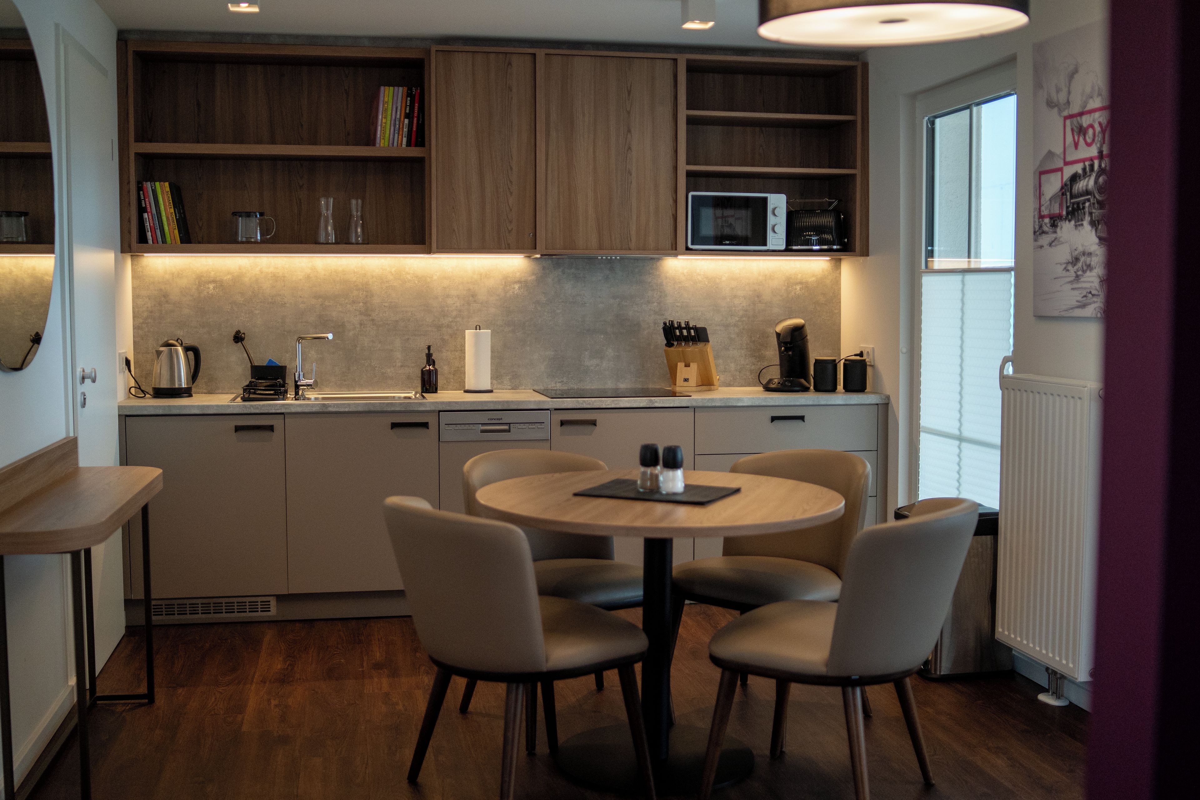 A modern kitchen with wooden cabinets, a built-in microwave, and a dining area with a round table and chairs.