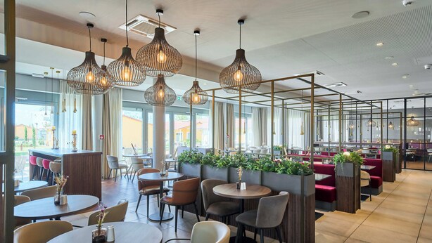 Un restaurante moderno con mesas redondas, asientos acolchados e iluminación colgante.