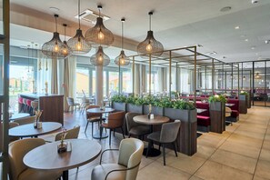 A modern restaurant with round tables, cushioned seating, and hanging pendant lights. - VOYA Hotel (Ringsheim)