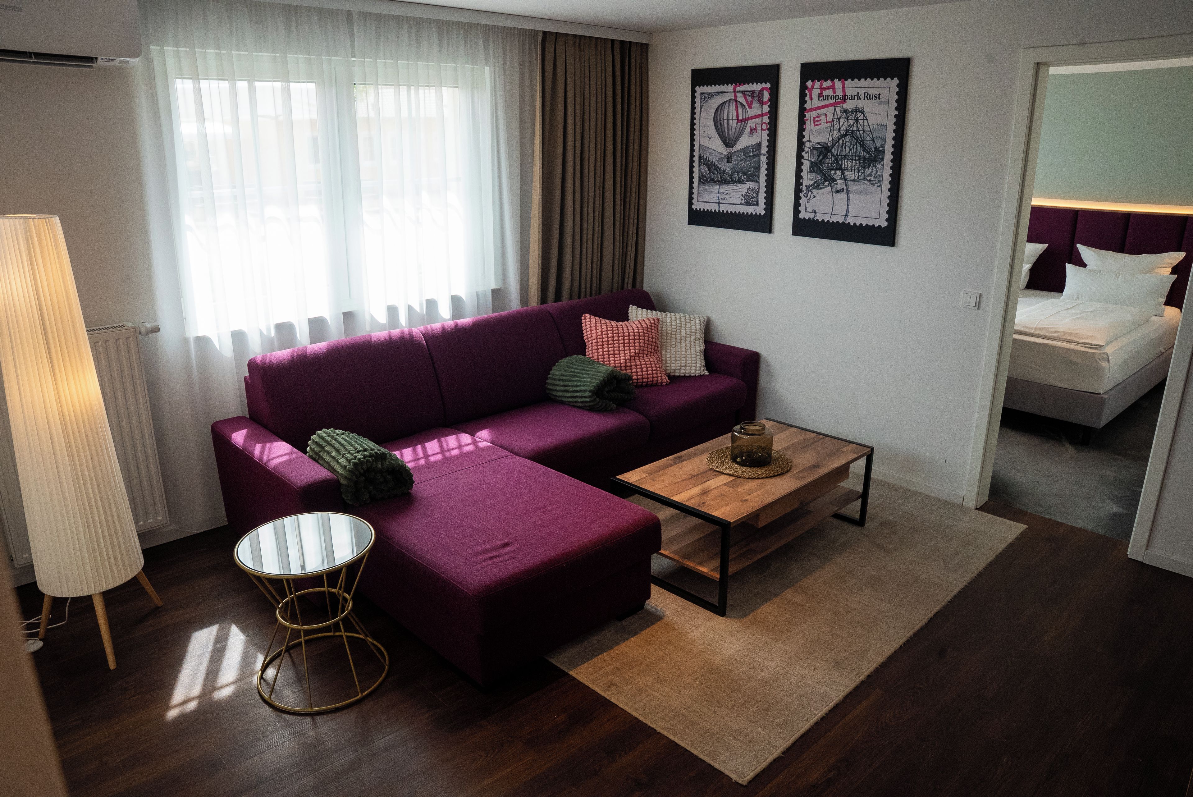 Una sala de estar moderna con un sofá morado, una mesa de centro de vidrio y piso de madera.