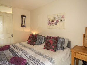 A bedroom with a bed, pillows, a wall mirror, and a floral artwork.