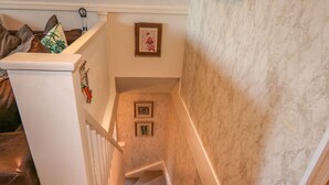 Una escalera alfombrada con barandilla blanca, una pared con cuadros enmarcados y una pared texturizada a la derecha.