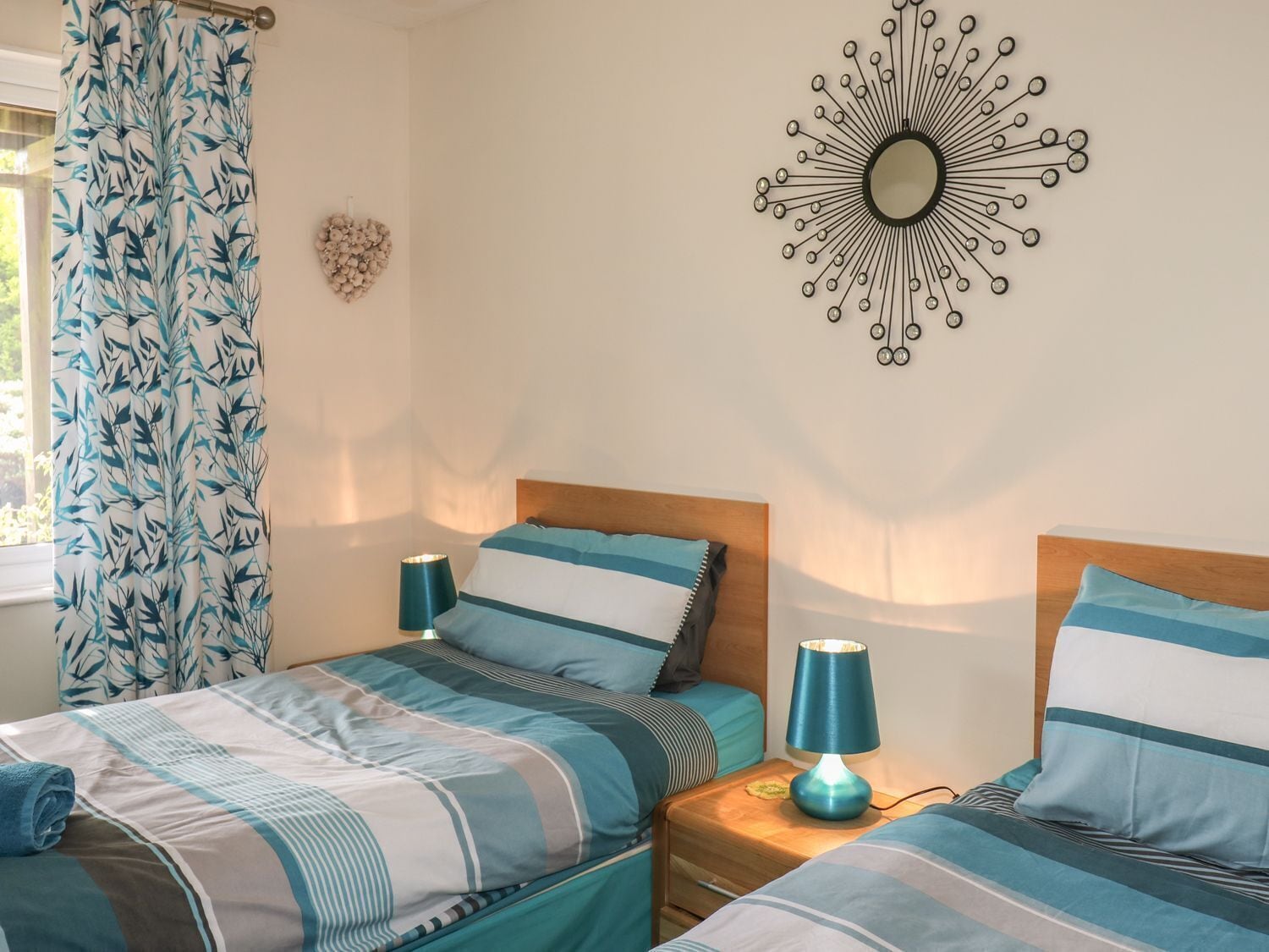 A bedroom with two beds, a wall-mounted mirror, and a decorative wall piece.