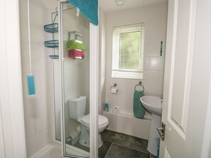 A compact bathroom with a glass shower enclosure, a toilet, a sink, and a window with blinds.