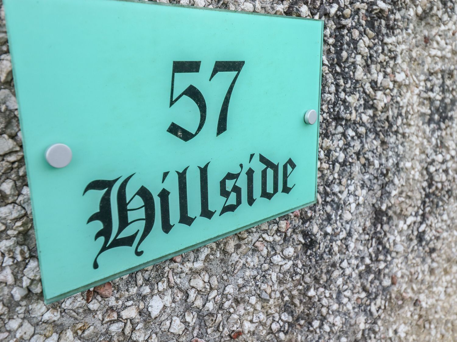 A teal sign with the number 57 and the word "Hillside" in a stylized font, mounted on a rough surface.