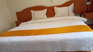 Un lit bien fait, avec une tête de lit en bois, une literie blanche et un élément décoratif jaune.