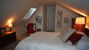 Quarto com cama grande, uma cadeira com um urso de pelúcia, luminária e obras de arte nas paredes.