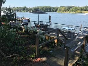Eine Holzterrasse mit Sitzgelegenheiten im Freien, mit Blick auf einen See mit Booten und einem Steg.