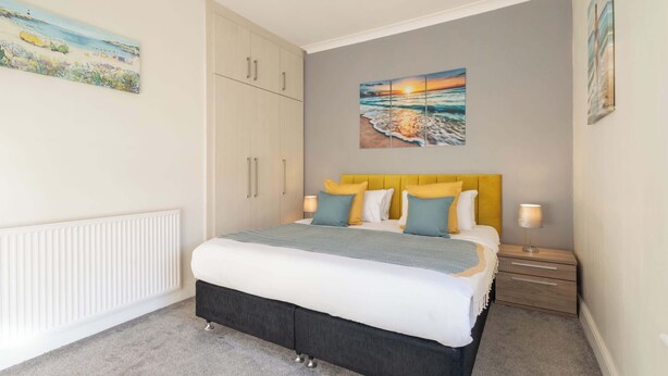 Une chambre à coucher avec un lit, des tables de chevet, un radiateur et des œuvres d’art accrochées aux murs.