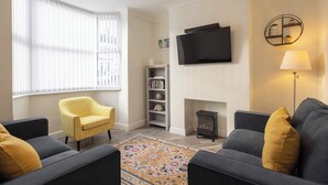 Un salon avec deux canapés, un fauteuil jaune, une bibliothèque, un téléviseur à écran plat et une cheminée.