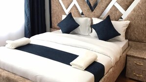 Een netjes opgemaakt bed met een hoofdbord met een geometrisch patroon, een nachtkastje met lades en een raam met gordijnen.