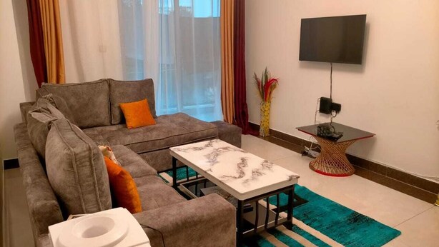 Een woonkamer met een grijze bank, een witte salontafel, een televisie aan de muur en een klein bijzettafeltje.