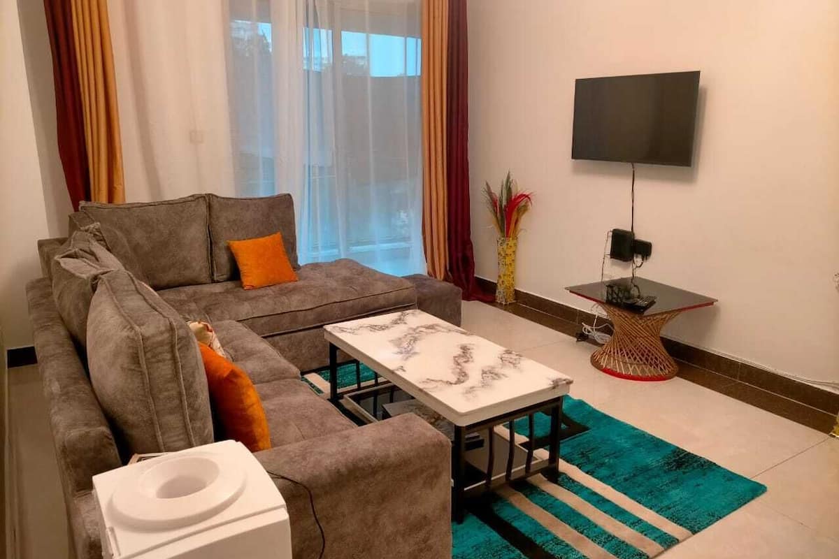A living room with a grey sofa, a white coffee table, a TV on the wall, and a small side table.