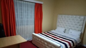 A hotel room with a bed, a desk, and a window with curtains. - Stay.Plus Karen Private House (Nairobi)