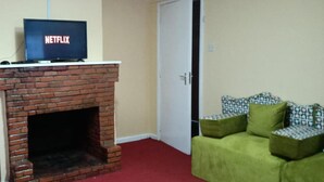 A living room with a brick fireplace, a green sofa, and a television displaying the Netflix logo. - Stay.Plus Karen Private House (Nairobi)
