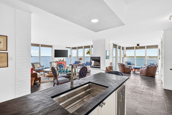 A spacious living area with a large window overlooking the sea, a fireplace, and a kitchen with a modern design.