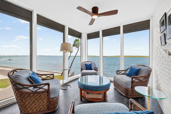 A room with wicker furniture, a glass table, and a ceiling fan.
