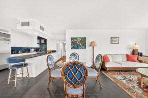 A modern kitchen with white cabinetry, a blue backsplash, and a dining area with wicker chairs and a glass table.