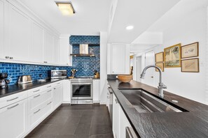 A modern kitchen with white cabinetry, a blue backsplash, and stainless steel appliances.
