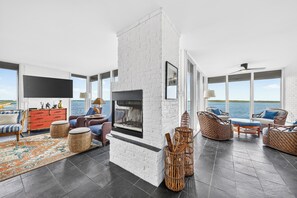 A spacious living room with a fireplace, comfortable seating, and large windows overlooking a body of water.