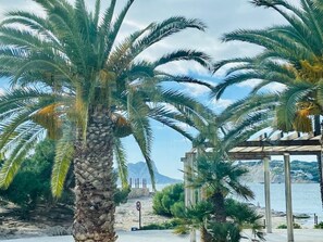 A beach scene with palm trees, a clear sky, and a view of the sea. - Stunning views, cycling base, pellet burner, pool! (Murla)