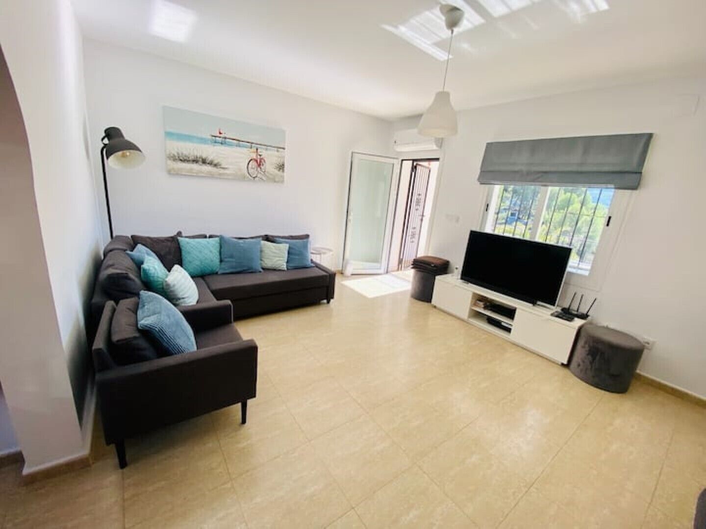 A modern living room with a sectional sofa, a flat-screen TV, and a large window.