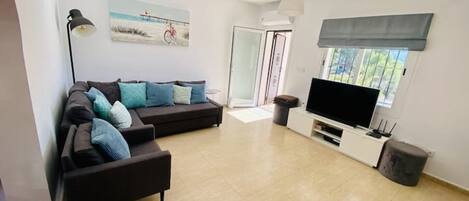 A modern living room with a sectional sofa, a flat-screen TV, and a large window.