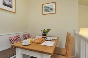 A dining area with a wooden table set for breakfast, including croissants, coffee, and juice. There are two framed pictures on the wall above the table.