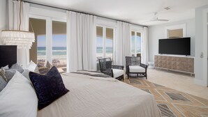 A hotel room with a large bed, two chairs, a TV, and a view of the beach. - Kamps Baai, Beachfront Home, Golf Cart, 2 Pools (Miramar Beach)