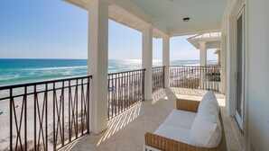 A covered balcony with a view of the ocean, white wicker furniture, and a metal railing. - Kamps Baai, Beachfront Home, Golf Cart, 2 Pools (Miramar Beach)
